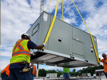 Crane lowering HVAC equipment onto a roof